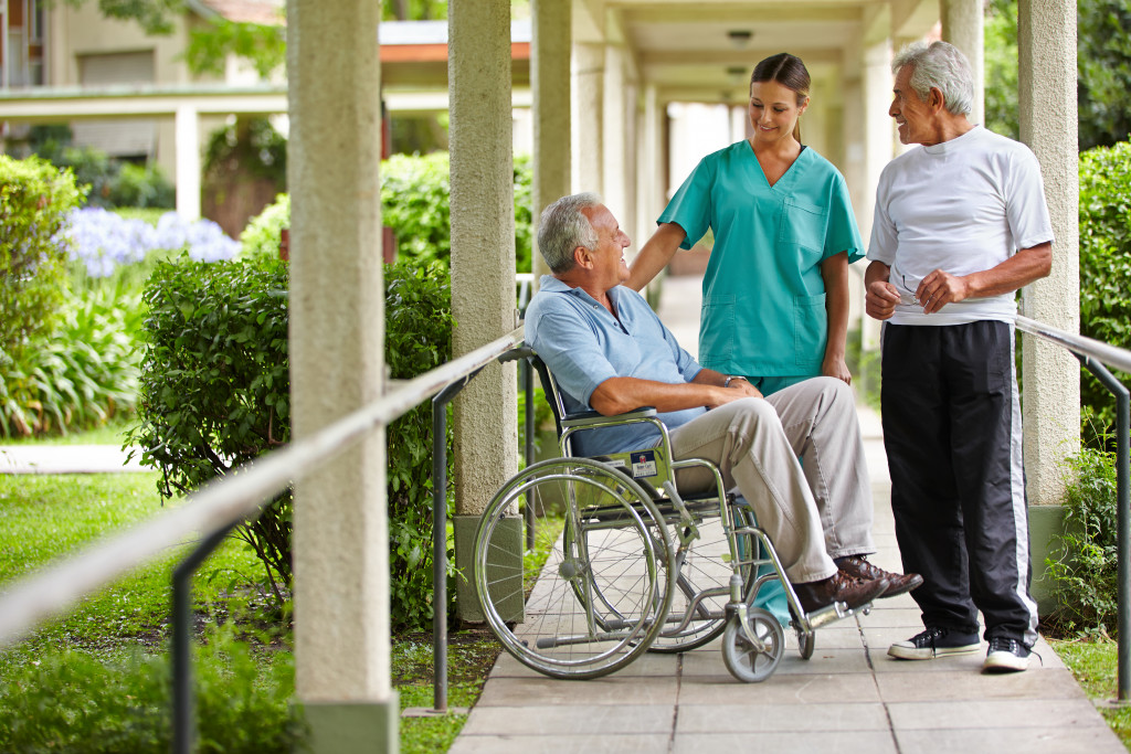 two senior males talking outdoors in a residential home with female patient